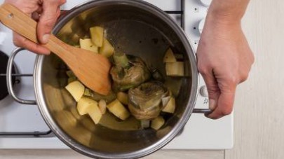 Pelate le patate e tagliatele a tocchetti, pulite i carciofi lasciandoli interi e fateli rosolare in una pentola dai bordi alti con poco olio extravergine di oliva.